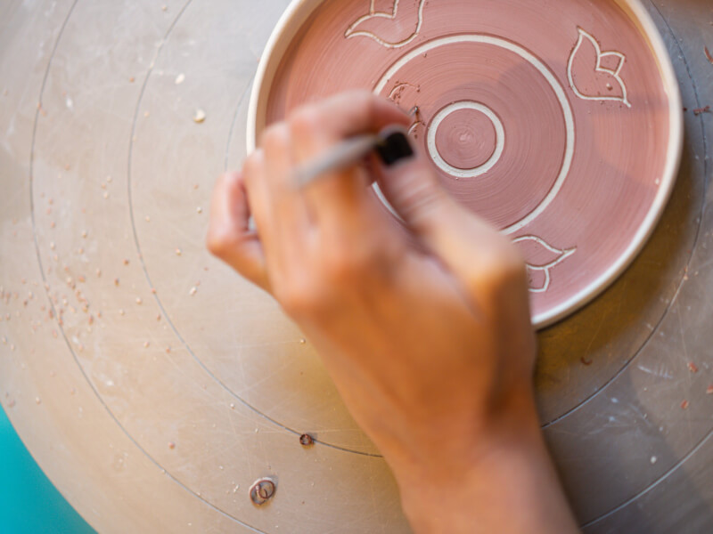 A close up of a person carving a pattern into a freshly painted plate at a pottery painting workshop in London